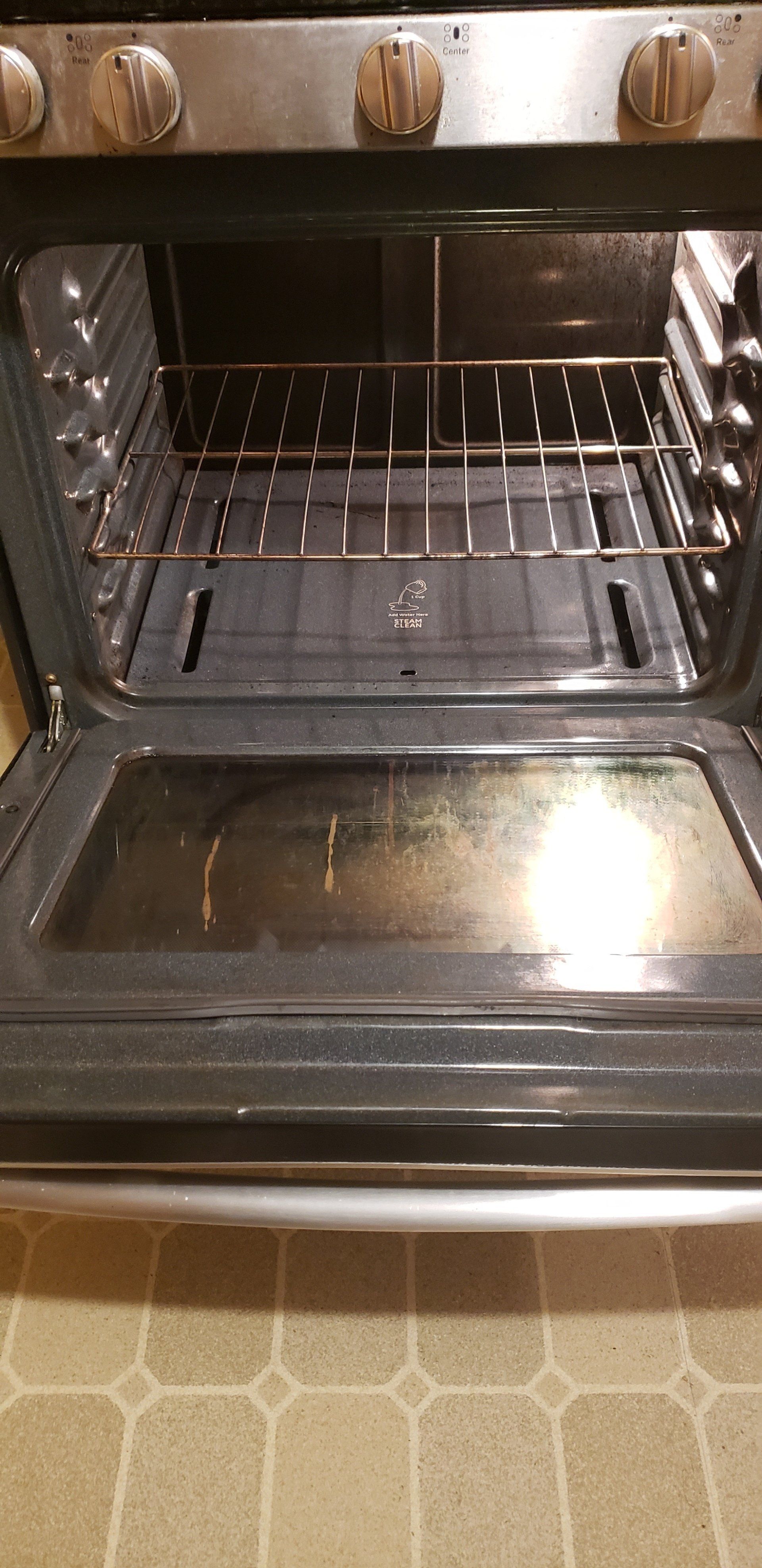 Open oven with racks inside, on patterned floor, controls at top.
