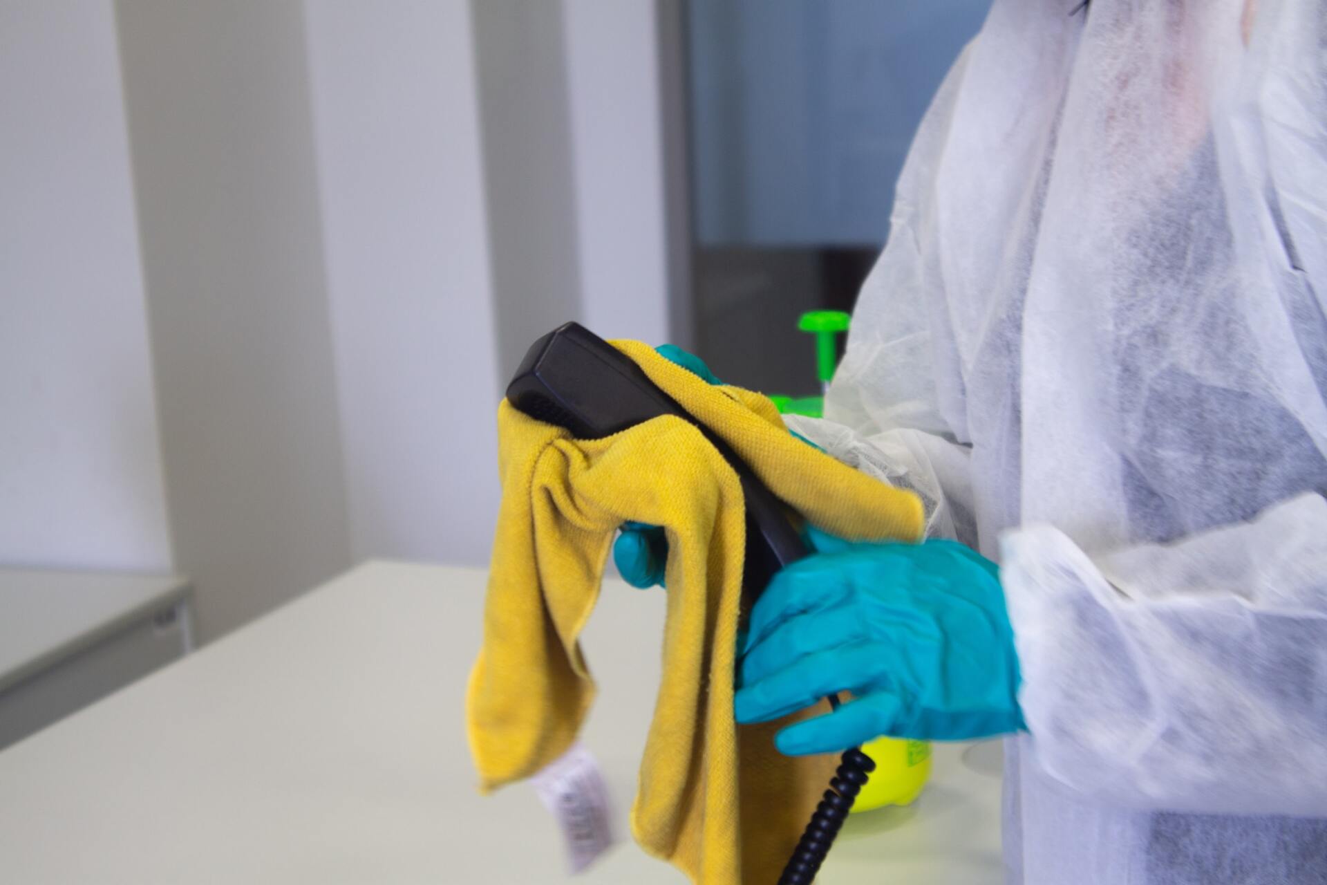 Person in protective suit and gloves wiping a black device with a yellow cloth.