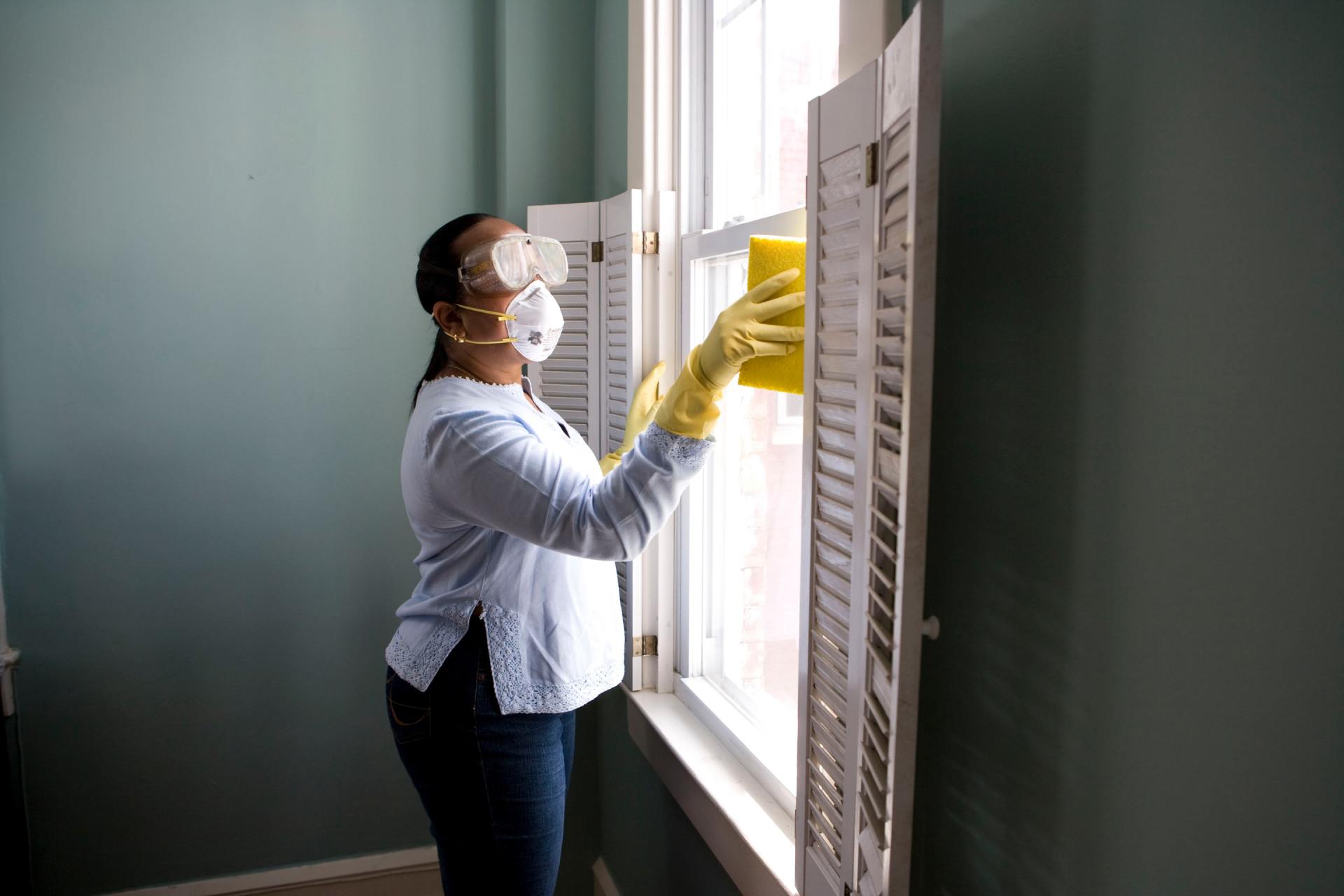 Person wearing protective gear cleans a window with shutters.