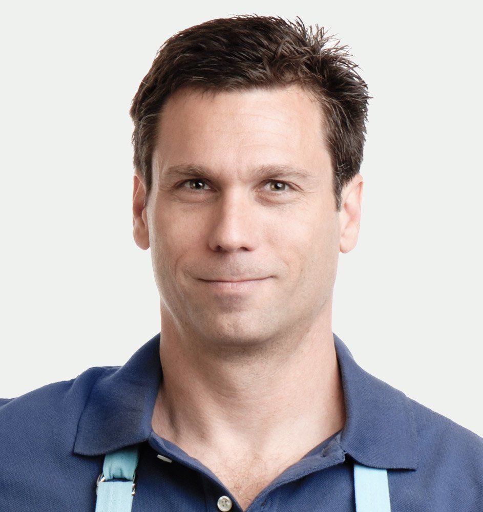 Man in a blue polo shirt and apron smiling at the camera.